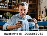 Shocked impressed caucasian middle-aged mature businessman freelancer boss self-employed man using smartphone, reading news, e-banking, loan, lottery winner in cafe restaurant