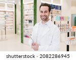 Small photo of Vertical portrait of caucasian male young pharmacist druggist in white medical coat holding clipboard with side effects, active substance, prescriptions standing at pharmacy drugstore