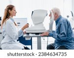 Woman oculist examining old man`s sight with ophthalmic tool in modern hospital clinic. Optician performing eyesight measurement for senior patient with myopia