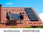 Two men installing new solar panels on the roof of a private house. Renewable energy concept and green energy abstract.