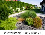 The frontyard of a modern house, garden details with colorful plants, dry grass beds surrounded by grey rocks.