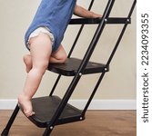 Small photo of Toddler baby climbs on the steps ladder. Child boy climbs up the stairs, stepladder. Kid age one year