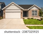 Looking at the front of a new one story brick ranch home with a gable roof in residential neighborhood subdivision with garage and double concrete driveway.