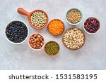   Legumes and beans assortment in different bowls on light stone background . Top view. Healthy vegan protein food.