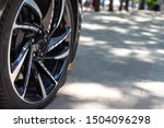 The front of the sports car. Wheel of a sports car on the background of a blurred sidewalk in a trendy metropolis area. Sports Car Alloy Wheel.