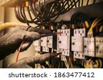 Close-up hand of electrical engineer using measuring equipment to checking electric current voltage at circuit breaker and cable wiring system for maintenance in main power distribution board.