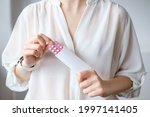 Small photo of Unrecognized woman in white blouse holding hormonal oral contraceptives in a pink blister. Concept of Hormonal methods of birth control. Estrogen and Progestin hormonal balance.