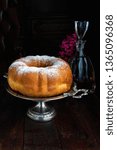 Small photo of Reindling - Austrian or German Easter festive yeasty baking on vintage metallic cake stand. There's a glass bottle and pink flowers next door on wooden background.