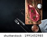 raw ribeye beef steak with Himalayan Pink salt, rosemary leaf herbs, and spices black pepper on a wooden cutting board. Top view on a dark background with copy space for your text