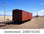 Small photo of Old Narrow Gauge Wooden Boxcar Sitting on a Stub Track in a Rail Yard with a Roundhouse in the Background