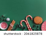 Green Christmas baking background with ginger cookies, sprinkles, candy canes, cinnamon sticks, cookie cutters and silver bauble. Xmas colors, flat lay.