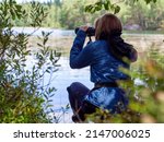 Young woman looking through binoculars at birds on the lake. Birdwatching, zoology, ecology. Research in nature, observation of animals Ornithology autumn bird migration selective focus, soft focus. 