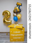 Small photo of A yellow box with balloons, a gold balloon number 2, a foil tractor balloon, the inscription on the balloon “Happy Birthday,” the inscription on the box: “Happy Birthday, son!” Balloons for a boy for