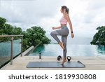 Small photo of Side view: slim female in fashion sportswear standing on mat on tiptoes and balancing while practicing yoga on balcony near infinity pool in the morning