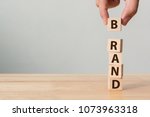 Hand of male putting wood cube block with word BRAND on wooden table. Brand building for success concept