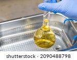 Small photo of Scientist in blue rubber puts a yellow solution in the flask for dissolving or extraction into ultrasound bath. Urea analysis. Clinical, toxicological and forensic analysis.