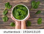 Fresh Organic Healthy Spinach in White Bowl Overhead Shot with White Female Hands Holding White Bowl on Wood Texture Table Background