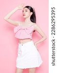 Small photo of Cute Asian woman model gathered in ponytail with korean makeup style on face have plump lips and clean fresh skin wearing pink camisole Raise her hand to cover the sun on isolated pink background.