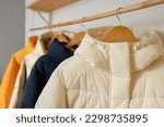 Winter clothes on a hanger in the room. A row of down jackets hang on a white background.