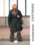 Small photo of Kyiv, Ukraine - August 21, 2022: Sagaydachnogo Str. Homeless redhead bearded man standing outdoors and begging. Sad charismatic beggar looking at the camera