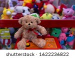 A cute teddy bear with a red scarf sits on a slot machine with his paw on the joystick against the background of soft toys.