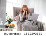 Small photo of Sitting in armchair. Red-haired woman sitting in armchair with laptop while being on sick leave