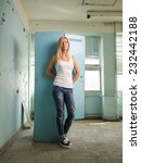 Small photo of Beautiful stylish daring hussy blond girl with straight hair in white T shirt and jeans confidently proudly looking at camera standing in room with old peeling walls full length