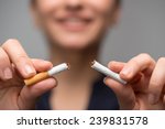 Close up portrait of young attractive woman breaking down cigarette to pieces. Studio shot selective focus isolated on grey. Addiction concept