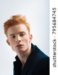 Small photo of Red-haired. Attractive humourless red-headed young man wearing a black jacket and looking in the distance and thinking