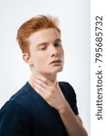 Small photo of Humourless. Attractive unsmiling red-haired young man touching his neck and wearing a black T-shirt and thinking