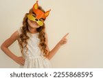 Small photo of A child in a carnival masquerade mask of a squirrel made of shiny foamiran. The child is fooling around in carnival masks. The mask is handmade. Girl getting ready for the carnival or masquerade.