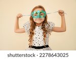 Small photo of The child tries on carnival masquerade masks. Little cute girl getting ready for carnival party, masquerade