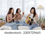 Small photo of young Asian women showcasing aesthetic enjoy a music session in university dormitory. woman is playing an acoustic guitar while the other sits on the bed using a hairbrush as a makeshift microphone
