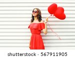 Fashion pretty happy smiling woman in red dress and sunglasses with air balloons heart shape looking up over white background