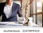 The Statue of Justice or lady justice with scales of justice on a table over blurred background of professional male lawyer or attorney.