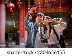 Cute and happy young Asian tourist couple taking their pictures with a smartphone while visiting a Chinese temple together.