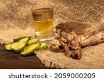 Small photo of A piece of homemade bacon with pepper, a glass of homemade moonshine and chopped pickles close-up, selective focus