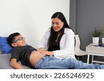 Small photo of Latin woman doctor checks the belly of a child in her office to rule out diseases such as appendicitis, gastroenteritis, hernia or ulcer