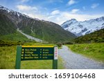 A sign to the kea point is a walking path to view the Muller Glacier and Muller Lakes in Mount Cook National Park. Rocky mountains and green grass in summer season in New Zealand.