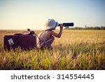 Picture of boy wearing pith helmet and plaid romper looking in spyglass in wheat field. Little explorer with camerabag and old suitcase on sunny countryside background.