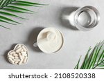 Small photo of Collagen powder in a bowl, collagen capsules and a glass of water on a gray background with palm leaves. A natural supplement. Fish based or plant based. Top view, flat lay.