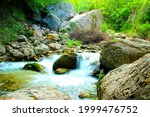 Small photo of Fresh scenery with lively green nature and gargantuan grey and brown rocks surrounding a glowing and translucent stream of pure mountainous waters from the Ambro river on a perfect summer day