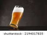 Small photo of Draught beer in glass on a black slate table and dark background. Tilted glass of fresh and cold beer on gray dark background. Selective focus
