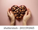 Valentine's Day chocolate candies in red heart shaped box, female hands