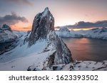 Scenic View from Mount Hesten on Iconic Mountain Segla at dawn in winter with snow in front of colorful sky and mountain range in background, Fjordgard, Senja, Norway