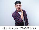 Small photo of Young handsome asian man wearing casual shirt and glasses over white background hand on mouth telling secret rumor, whispering malicious talk conversation