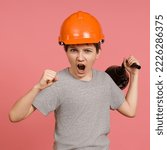 Small photo of combat screaming boy in a gray t-shirt with a helmet on his head brandishes a big funnel and shows his fist, pink background