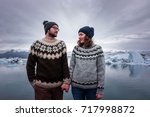 Man and woman in traditional handmade sweaters holding hands in front of glacier lagoon in Iceland