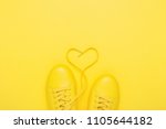 Pair of yellow shoes with heart made of shoelaces on yellow background. Trendy summer color, monochrome image.