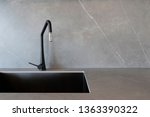 A black sink and a matt-finish black faucet set against grey surfaces made of porcelain slabs that mimic the look of natural stones. 